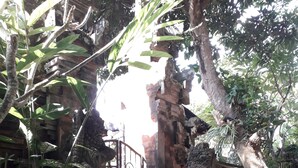 A stone pathway leading to a temple entrance with intricate carvings and a metal gate. - Widi House (Ubud)