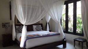 A bedroom with a four-poster bed, white bedding, a colorful quilt, and a view of greenery through the window. - Widi House (Ubud)