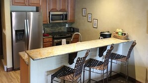 A kitchen with wooden cabinets, stainless steel appliances, a granite countertop, and a bar area with wicker chairs. - Book your Winter get away now (Avon)