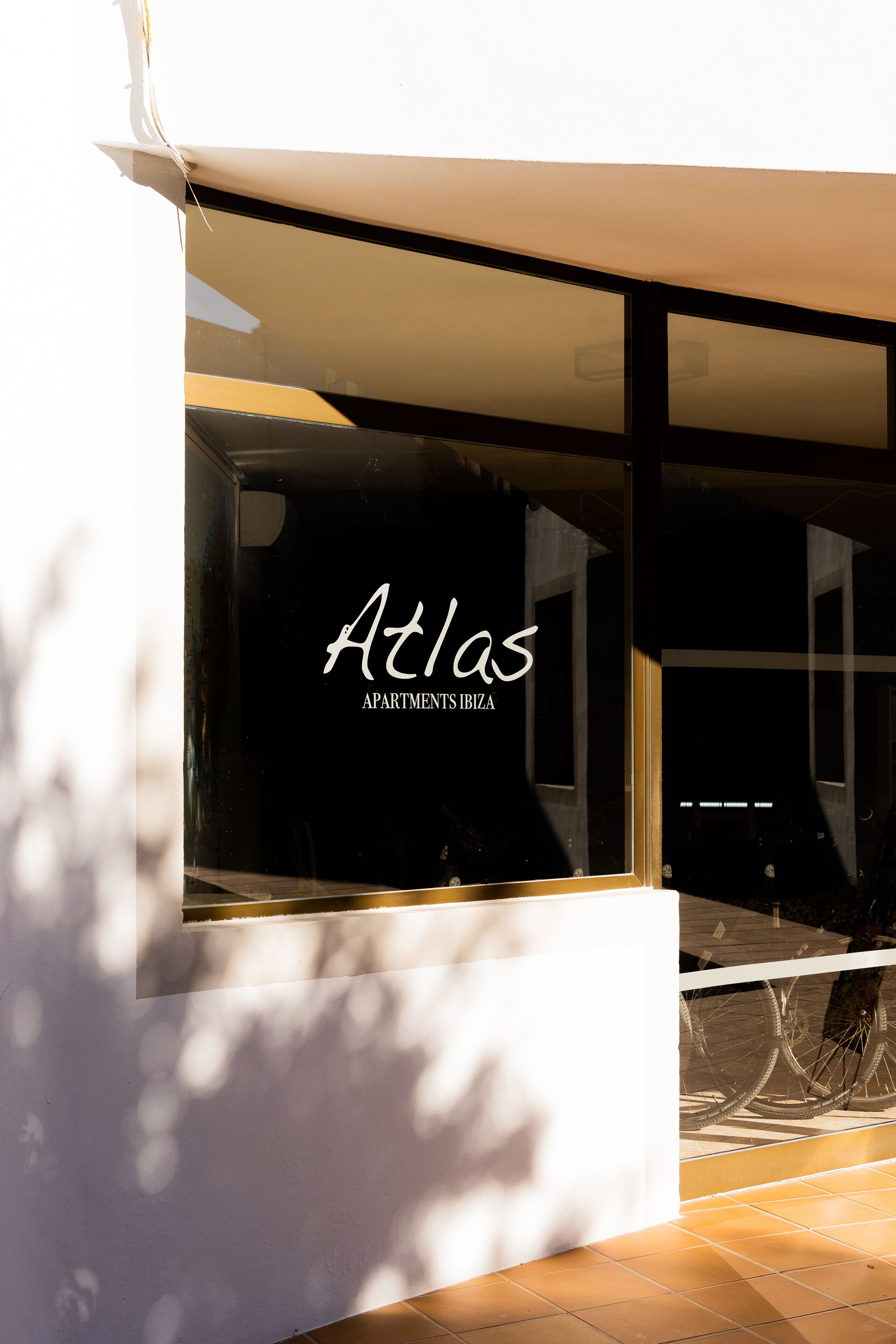 En moderne bygning med store vinduer og teksten "Atlas Apartments Ibiza" i vinduet.