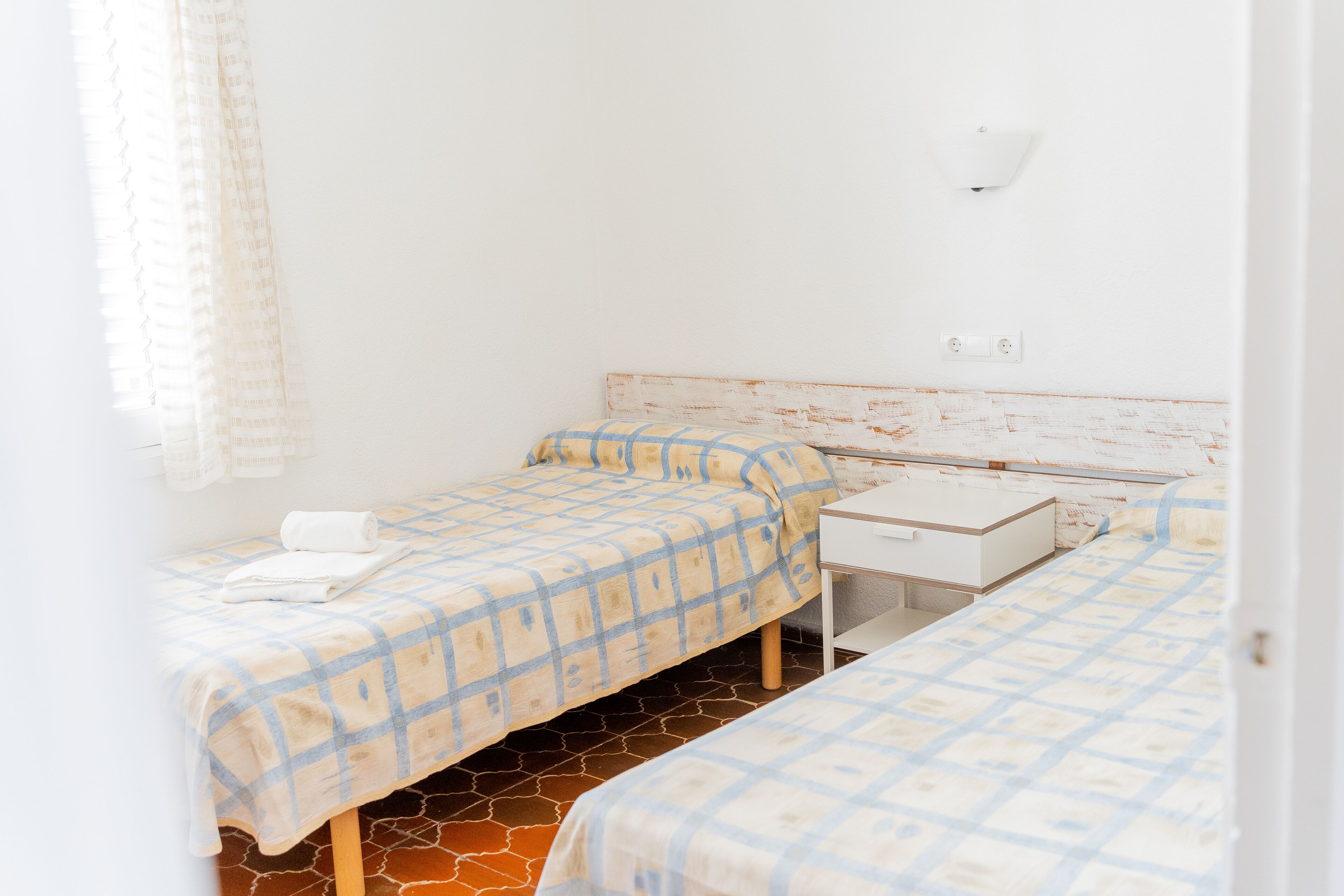 A room with two beds, a small desk, and a white wall.