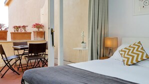 Une chambre d’hôtel avec un lit, une petite table avec des chaises, une plante en pot, une lampe et une vue sur l’extérieur.