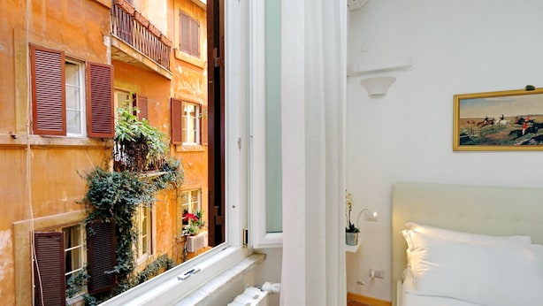 A room with a view of a building with balconies, a bed, a painting, and a potted plant. - Casa Navona - My Extra Home (Rome)