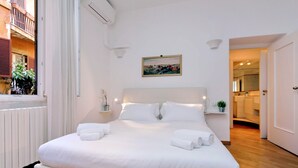 A neatly made bed with white linens and towels, a painting on the wall, and a view of the bathroom through an open door. - Casa Navona - My Extra Home (Rome)
