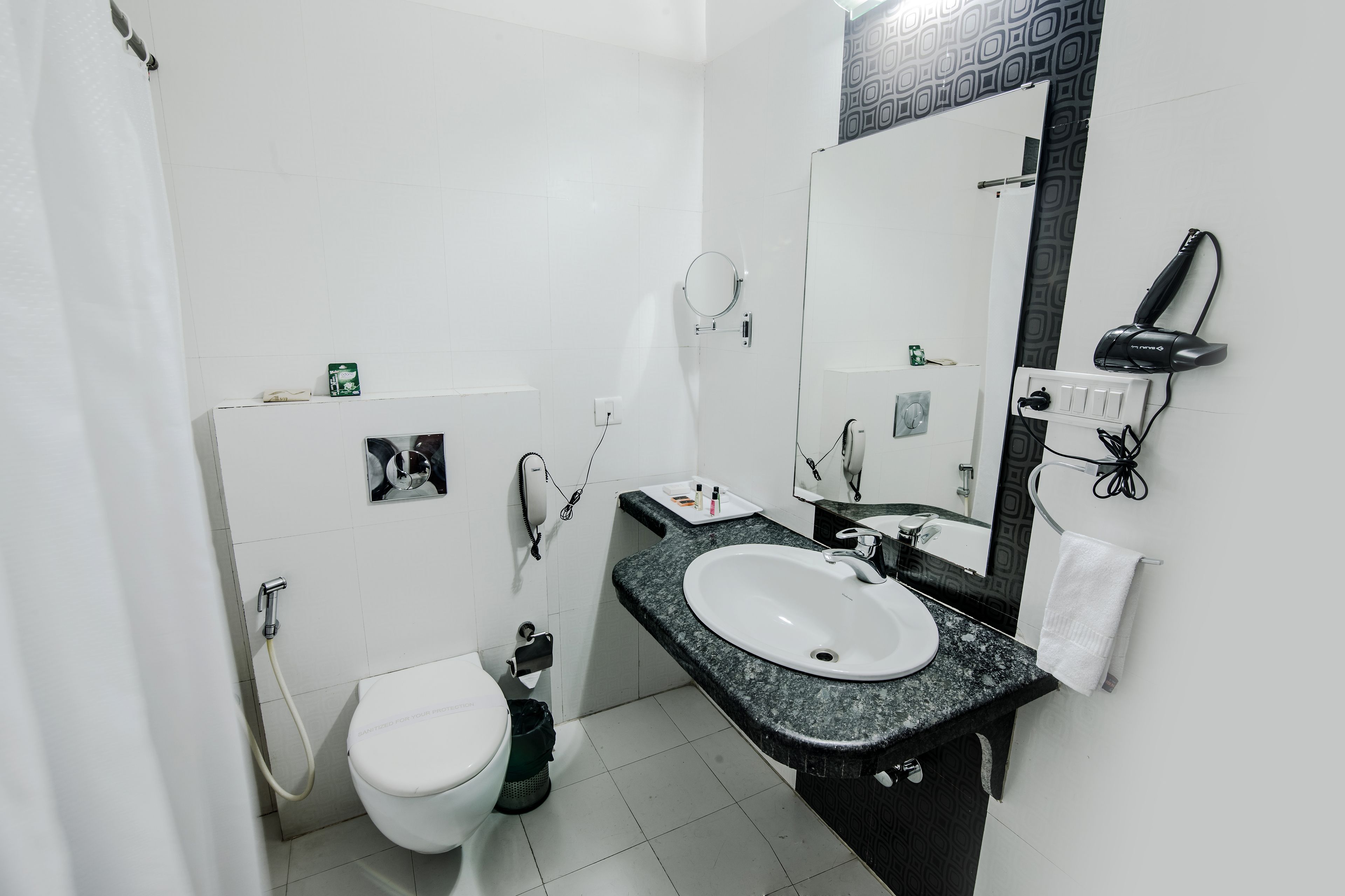 A bathroom with a white toilet, a sink with a black countertop, a mirror, and a hairdryer on the wall.