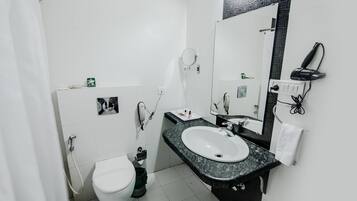 A bathroom with a white toilet, a sink with a black countertop, a mirror, and a hairdryer on the wall.