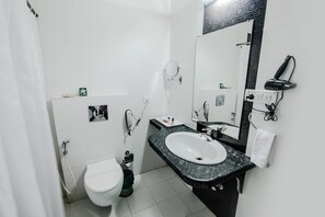 A bathroom with a white toilet, a sink with a black countertop, a mirror, and a hairdryer on the wall. - Hotel AVN Grand (Ranchi)