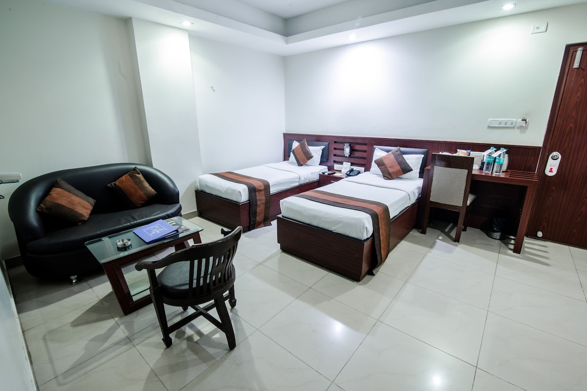 Una habitación de hotel con dos camas individuales, un sofá, una mesita y una silla.