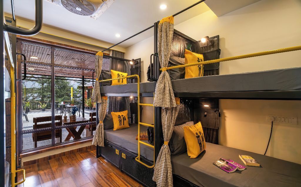 A compact hotel room with bunk beds, a small table, and a window overlooking a patio area.