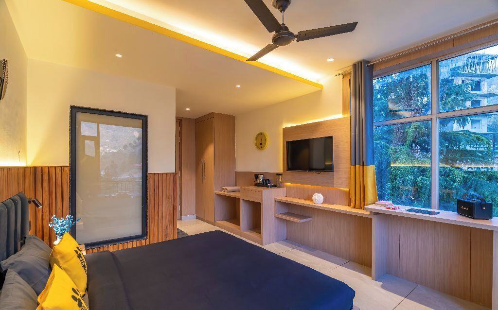 A modern bedroom with a bed, a TV, a ceiling fan, and a window with a view of greenery.