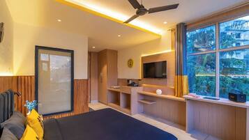 A modern bedroom with a bed, a TV, a ceiling fan, and a window with a view of greenery.