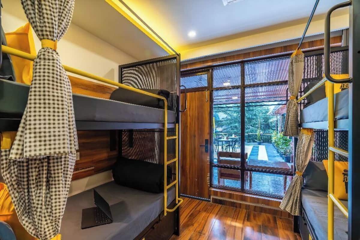 Une chambre avec des lits superposés, un plancher en bois, une fenêtre donnant sur l’extérieur et un luminaire suspendu.