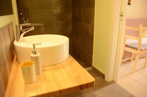 Une salle de bain avec un lavabo rond, un plan de toilette en bois, un porte-brosse à dents et un gobelet.