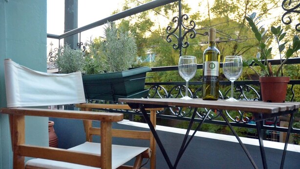 A balcony with a wooden chair, a table, two wine glasses, a bottle of wine, and potted plants. - Circle Inn (Athens)