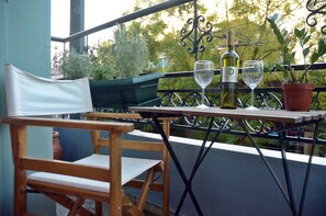 Un balcon avec une chaise en bois, une table, deux verres à vin, une bouteille de vin et des plantes en pot.
