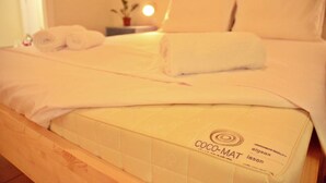 A neatly made bed with a white duvet and two rolled towels, a bedside table with a lamp, and a small potted plant. - Circle Inn (Athens)