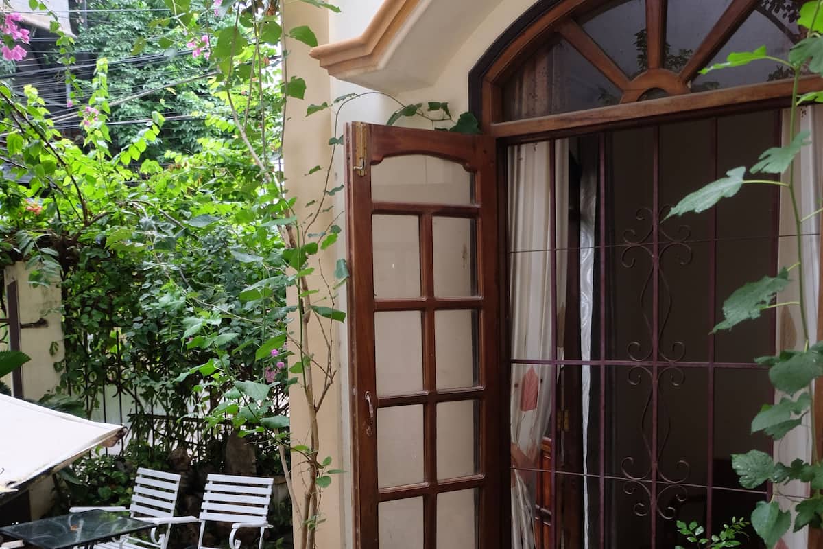 A courtyard with a table and chairs, surrounded by potted plants and a window with a decorative grille.