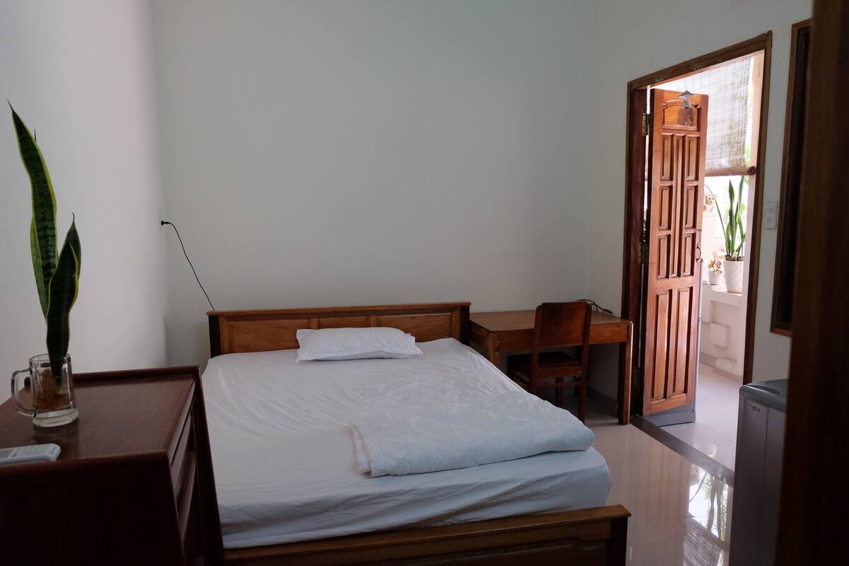 A neatly arranged bedroom with a bed, bedside table, and a desk.