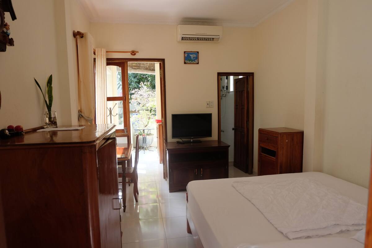 A bedroom with a bed, a TV, a wooden cabinet, and a desk with a chair.