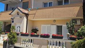 A multi-story building with balconies, potted plants, and a tiled ground floor. - Apartmani M&L (Medulin)