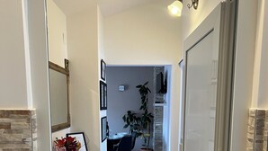 An interior hallway leading to a dining area with a table and chairs, a potted plant, and a mirror on the left. - Apartmani M&L (Medulin)