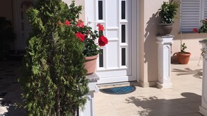 A building with a white door, a blue sign above it, and potted plants in front. - Apartmani M&L (Medulin)