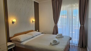 A neatly made bed with a wooden headboard, a bedside table, and a wall-mounted light fixture. - Apartmani M&L (Medulin)
