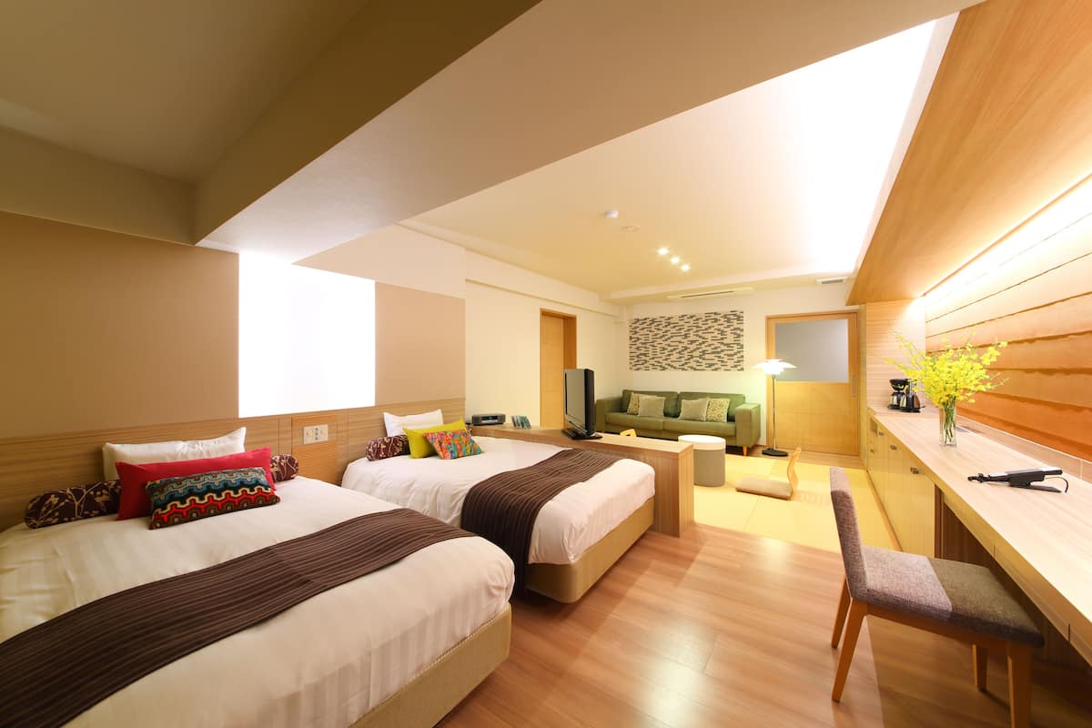 A hotel room with two beds, a desk, and a seating area.