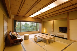 A traditional Japanese-style room with tatami flooring, a low wooden table, a sofa with cushions, a television, and a window with a view of trees. - Bansyoukaku Shikishima (Ureshino)