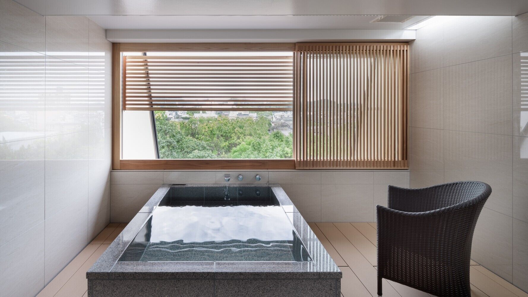 A modern bathroom with a glass-enclosed hot tub, a wooden window with blinds, and a wicker chair.