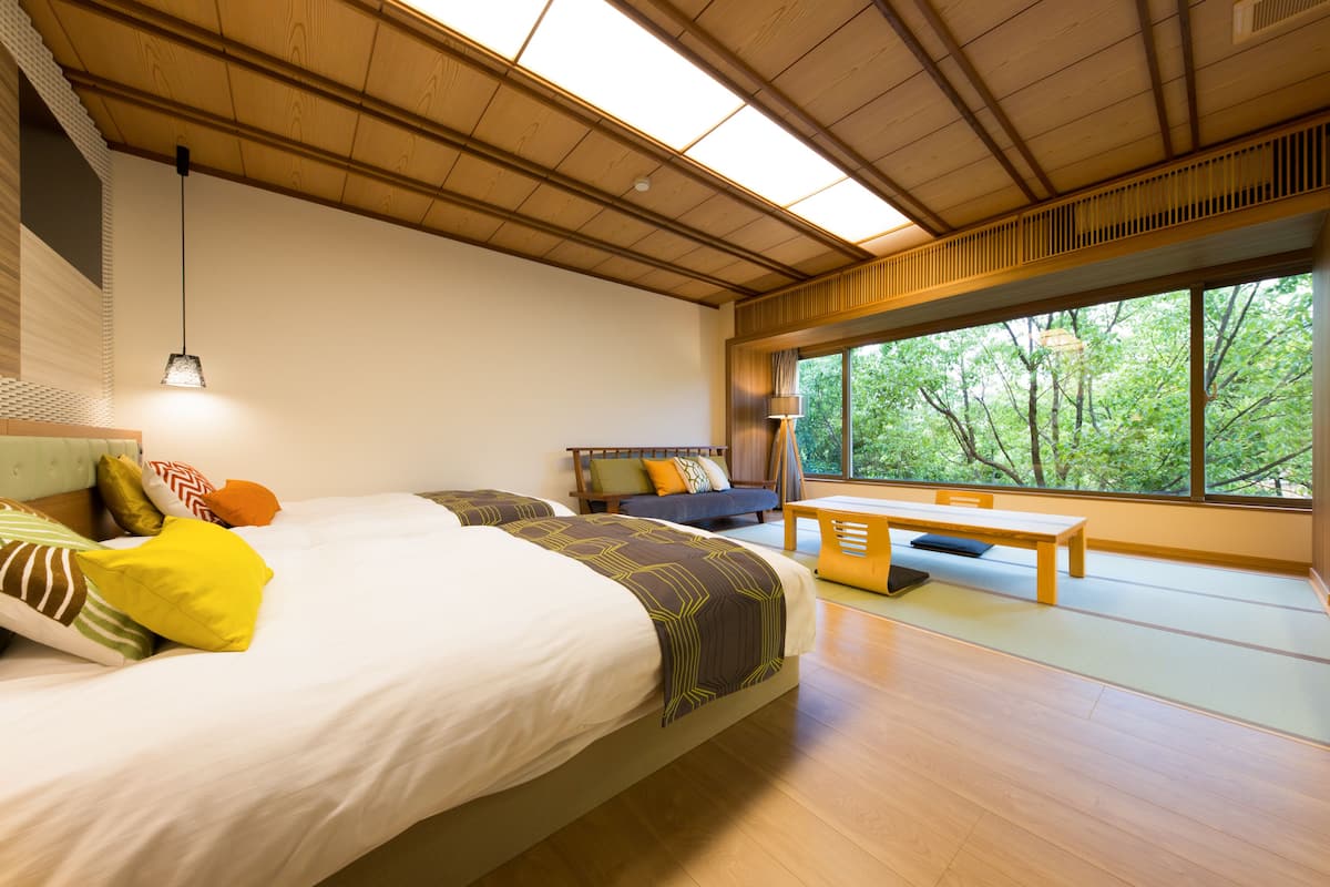 A bedroom with a large bed, a bench, and a view of trees through a window.