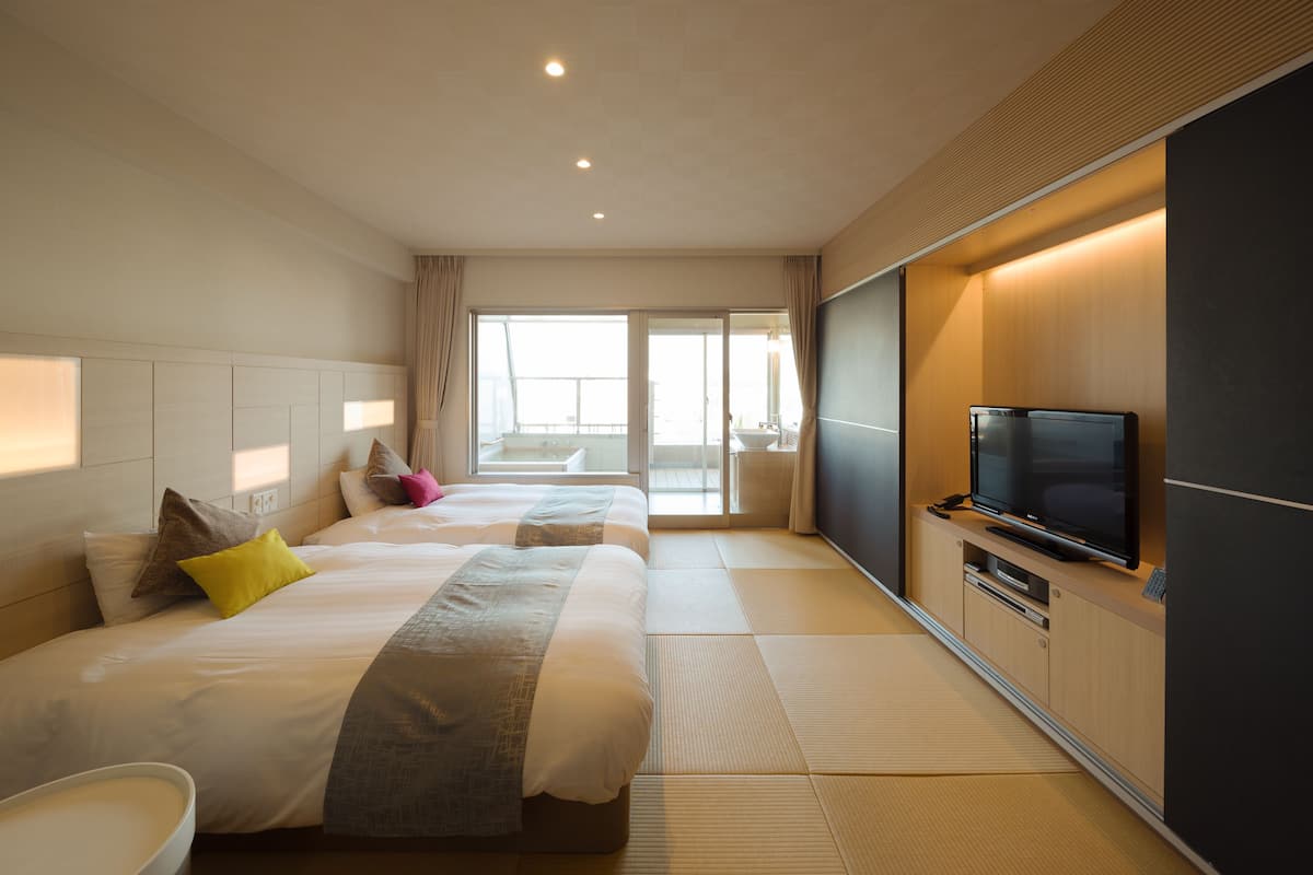 A hotel room with two beds, a TV, and a view of the balcony.
