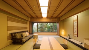 A traditional Japanese room with tatami flooring, a low table, a sofa, and a view of greenery outside. - Bansyoukaku Shikishima (Ureshino)
