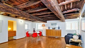 Um quarto amplo com piso de madeira, área de jantar com cadeiras vermelhas, um armário de madeira e uma poltrona de couro preta.