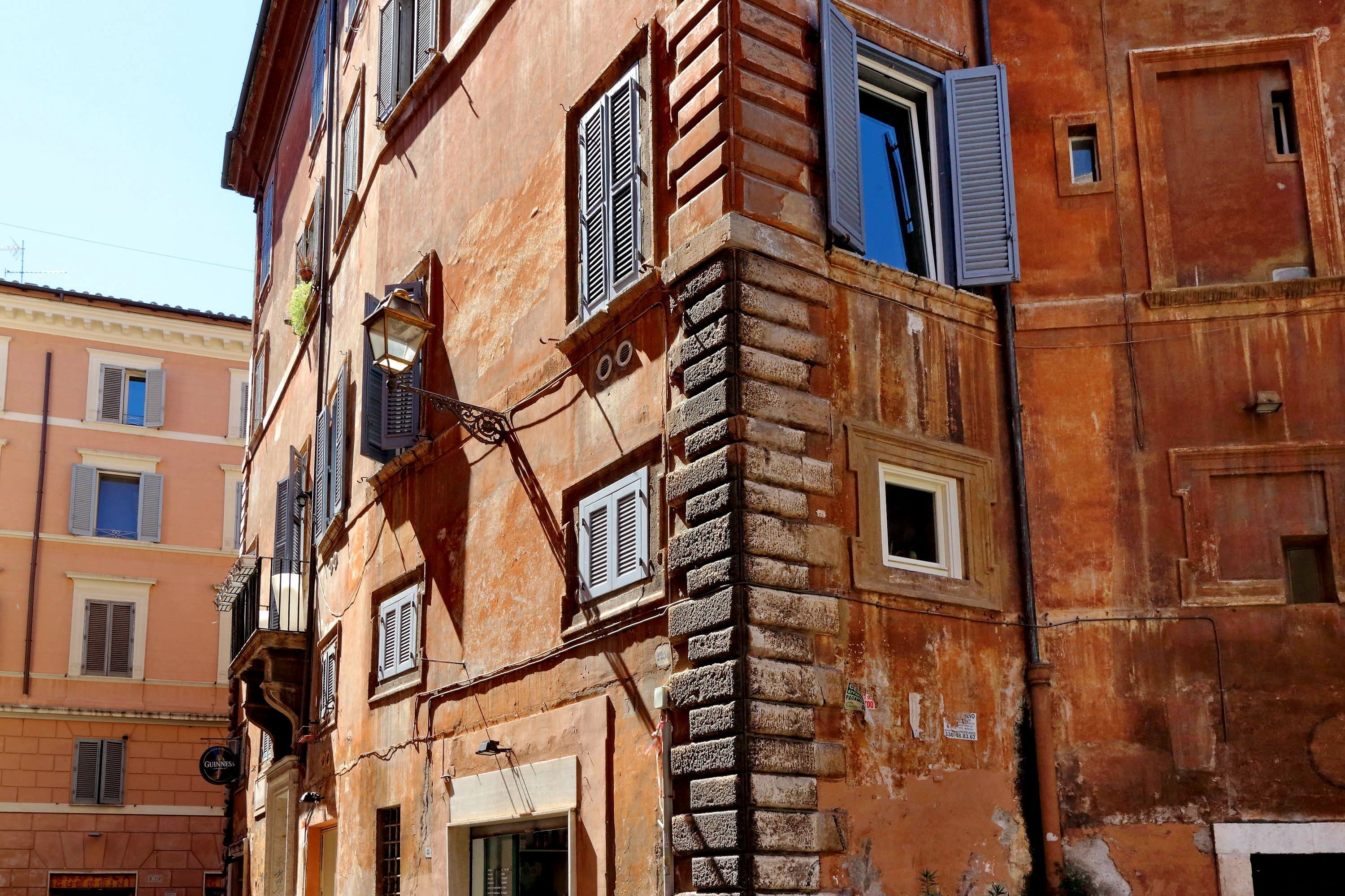 Un immeuble à plusieurs étages, dont la façade présente un mélange de styles de fenêtres et de volets, et qui se distingue par une architecture traditionnelle intégrant des éléments en pierre et en brique.