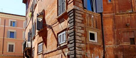 Un immeuble à plusieurs étages, dont la façade présente un mélange de styles de fenêtres et de volets, et qui se distingue par une architecture traditionnelle intégrant des éléments en pierre et en brique.