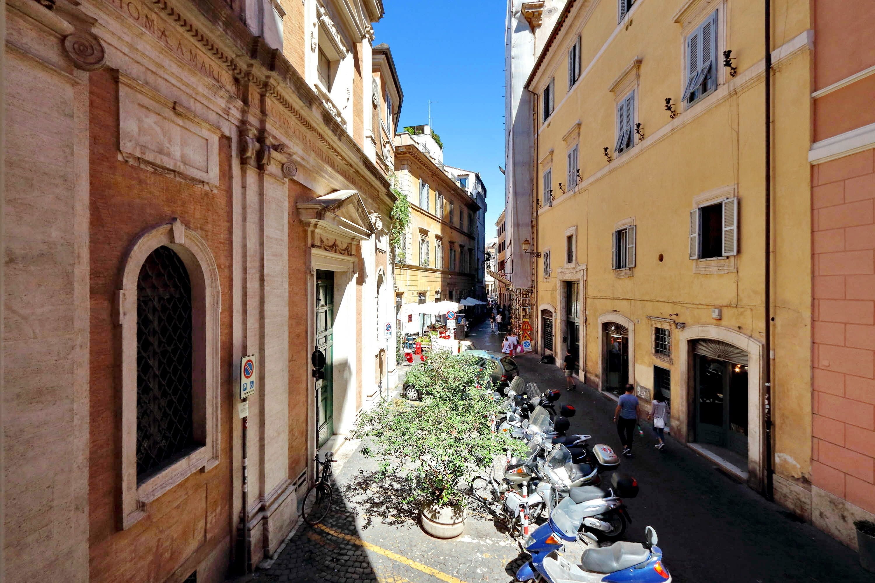 A narrow street with parked scooters and a potted plant.