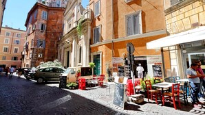 A cobblestone street with outdoor seating, a café, and a restaurant with a sign advertising 'Pizzeria'. - Parione Charme - My Extra Home (Rome)