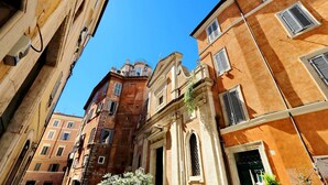 Uma rua estreita com edifícios históricos, incluindo uma igreja imponente com cúpula e janelas em arco.