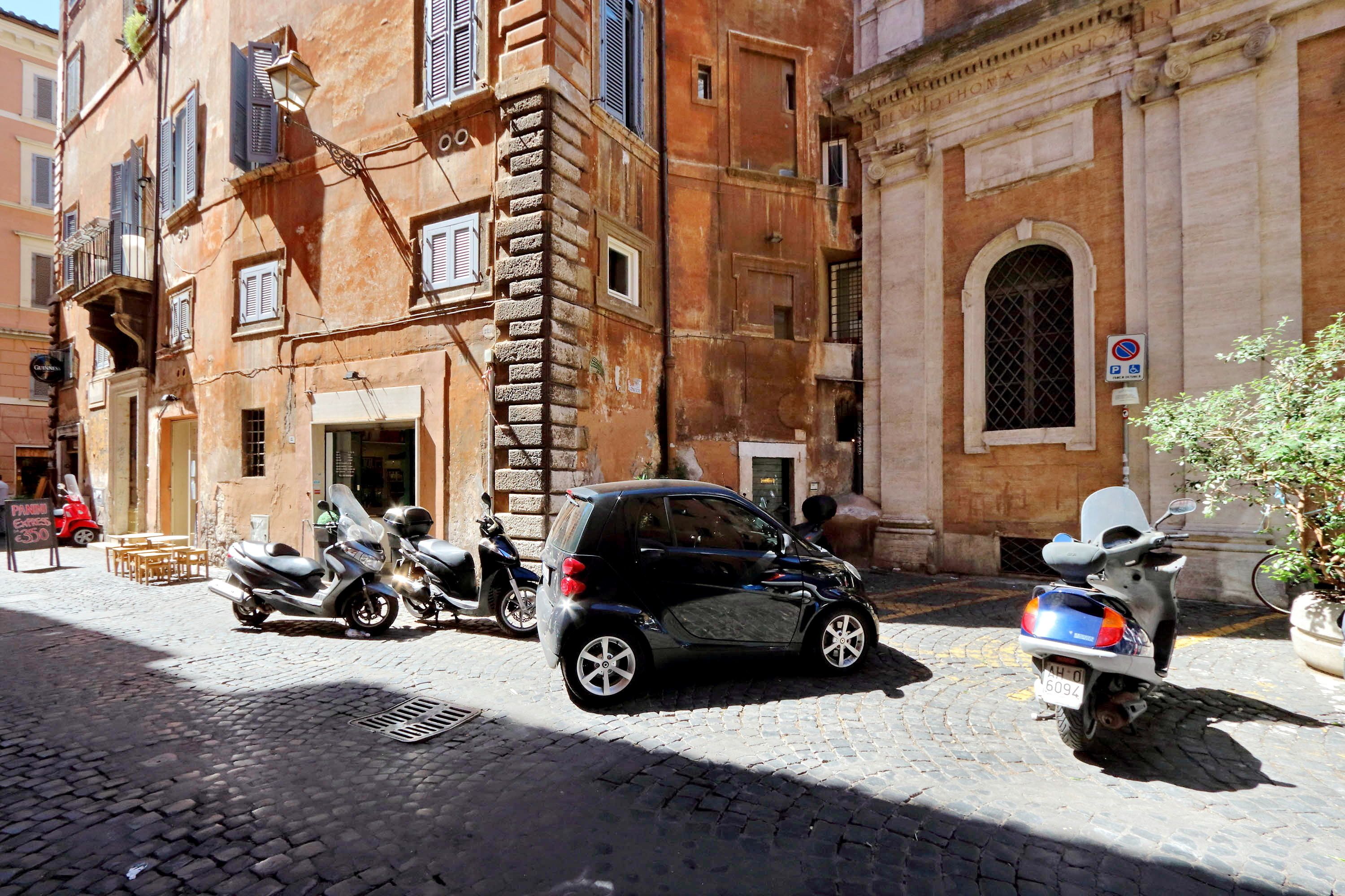 A cobblestone street with parked scooters and a car.