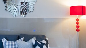 Ett modernt vardagsrum med ett reflekterande konstverk på väggen, en röd golvlampa och en soffa med mönstrade kuddar.
