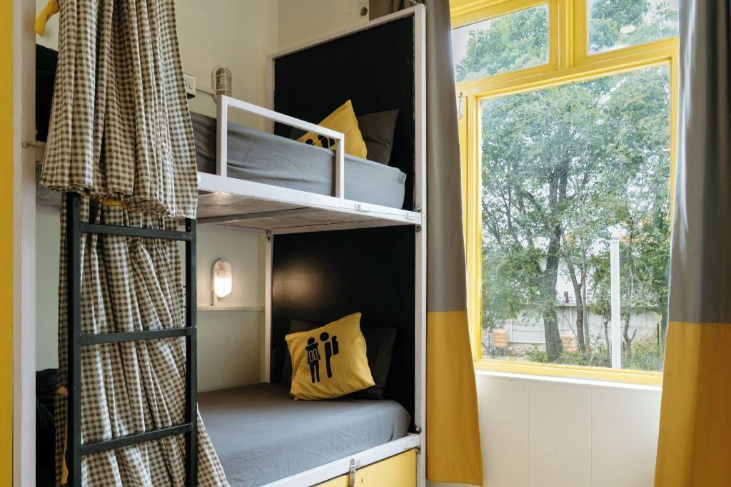 Una habitación tipo dormitorio con literas, una ventana con vistas a árboles y una cortina.