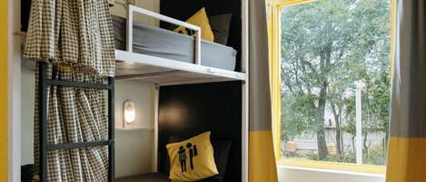 Una habitación tipo dormitorio con literas, una ventana con vistas a árboles y una cortina.