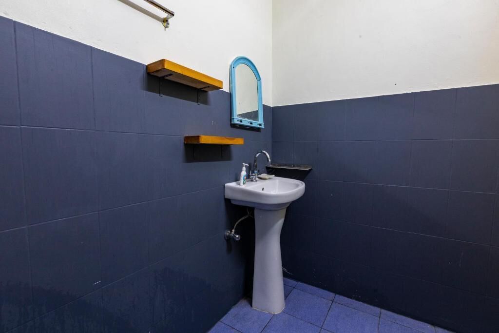 Un baño con lavamanos blanco, paredes con azulejos azules y un espejo encima.