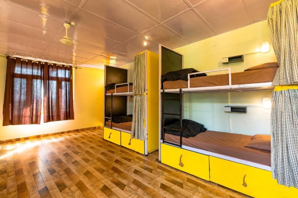 A dormitory room with bunk beds, a window with curtains, and a wooden floor.