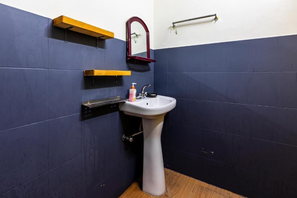 A bathroom with a white pedestal sink, dark blue walls, a wooden shelf, and a mirror.