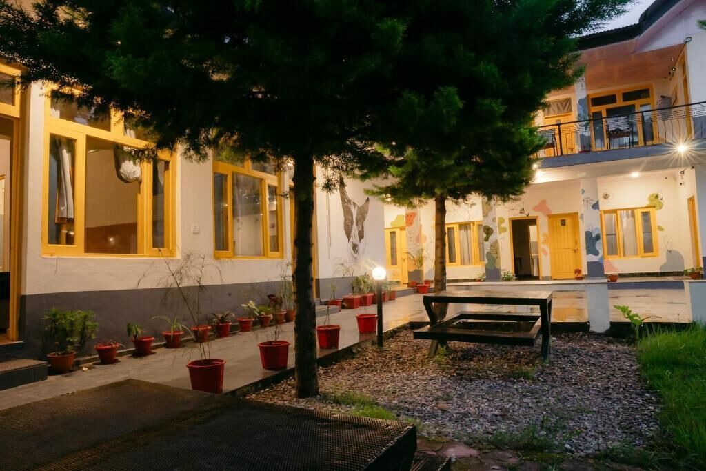 A courtyard with a bench, potted plants, and a building with yellow-framed windows.