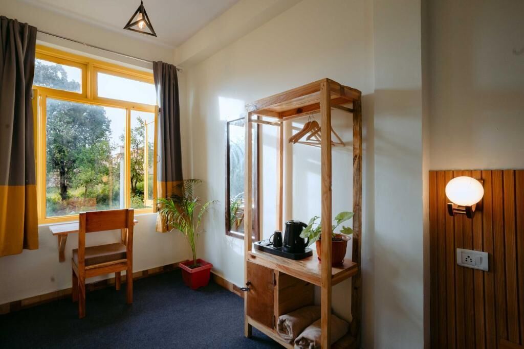 A room with a wooden desk, a chair, a hanging plant, a shelf with a kettle, and a window with curtains.