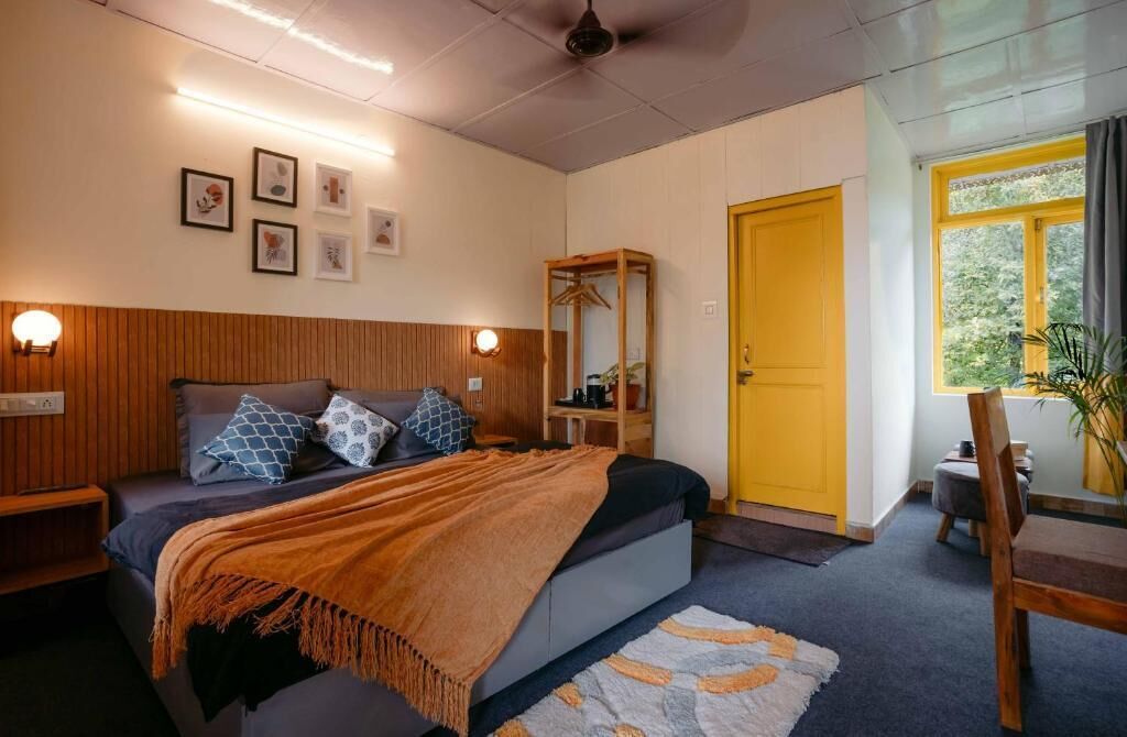 A bedroom with a bed, bedside tables, a wooden wardrobe, a mirror, and a window with a view of greenery.