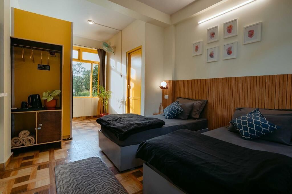 Une chambre d’hôtel avec deux lits, une tête de lit en bois, un petit coin salon, une armoire et une fenêtre donnant sur un paysage verdoyant.